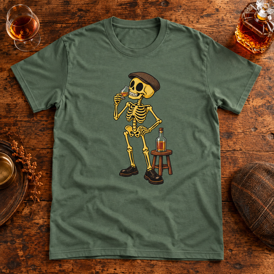 Themed flat-lay photograph of Cognac Lover - T-shirt featuring a flat-capped skeleton savouring a cognac glass beside a bottle on a stool.