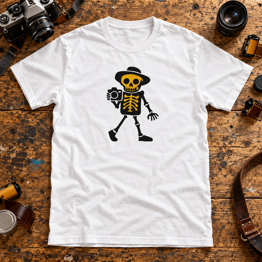 White Valokuvaaja photographer skeleton T-shirt on a wooden table with cameras, lenses and film rolls.