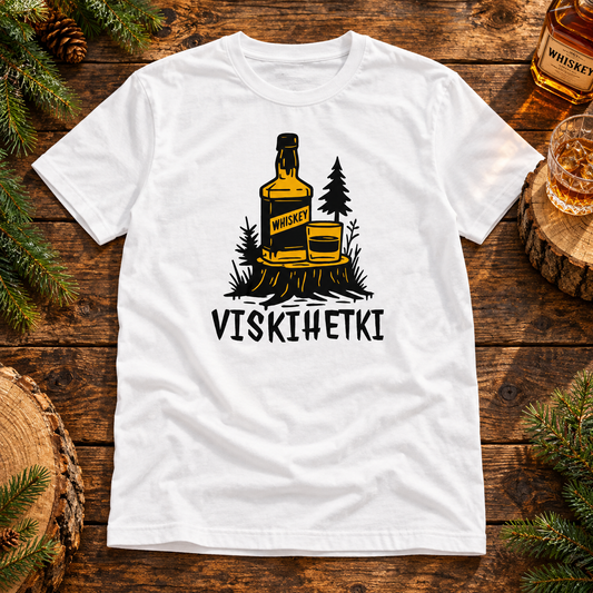 White Viskihetki T-shirt with a whiskey bottle and glass print on a wooden table with whiskey and pine sprigs.